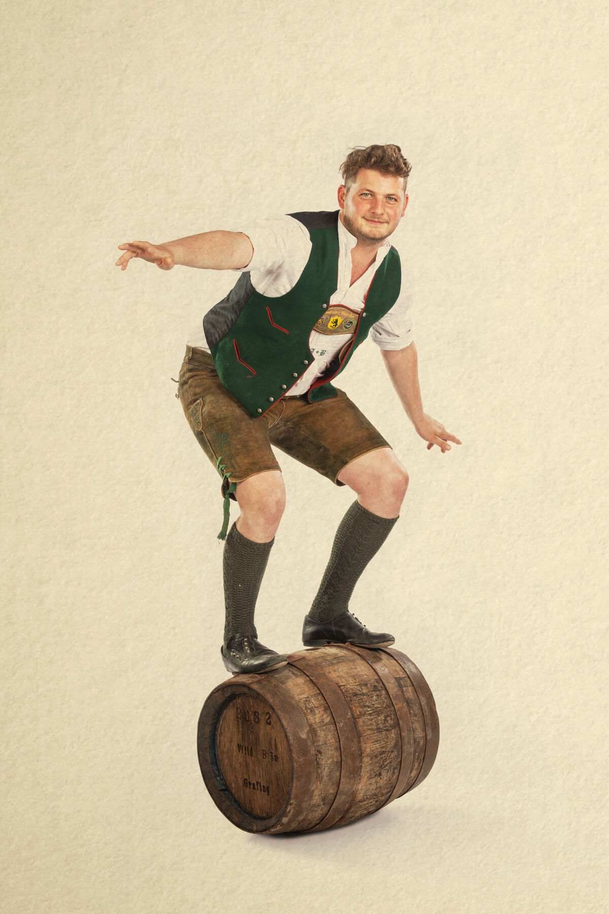Junger Mann in Tracht, der auf einem Bierfass balanciert. Fass-Surfer. Wildbräu Fotoshooting für Kampagne. Werbekampagne. Wild und urbayerisch. Humor Werbeagentur Werbung Bier.